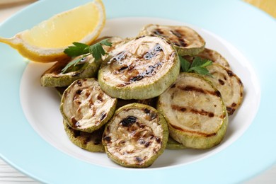 Tasty grilled zucchini slices with lemon and parsley on white table, closeup