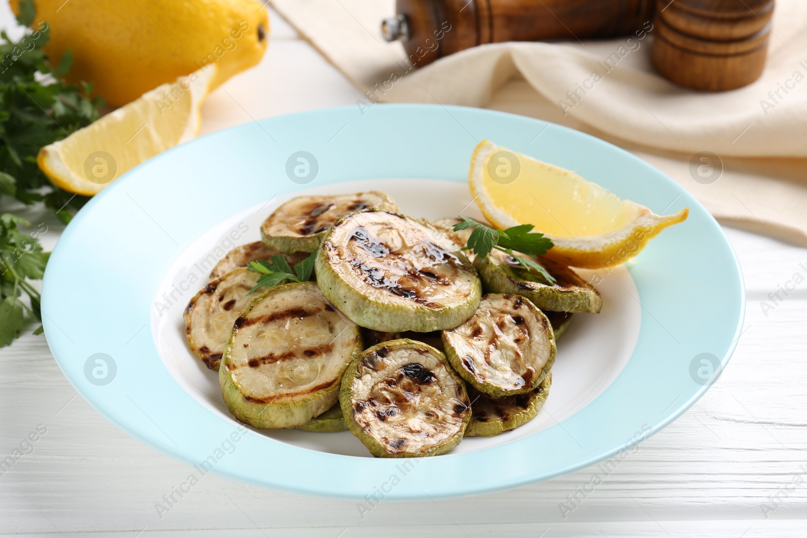 Photo of Tasty grilled zucchini slices with lemon and parsley on white wooden table