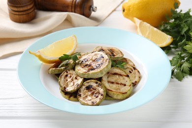 Tasty grilled zucchini slices with lemon and parsley on white wooden table