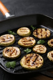 Photo of Tasty grilled zucchini slices with parsley in frying pan on grey table, closeup