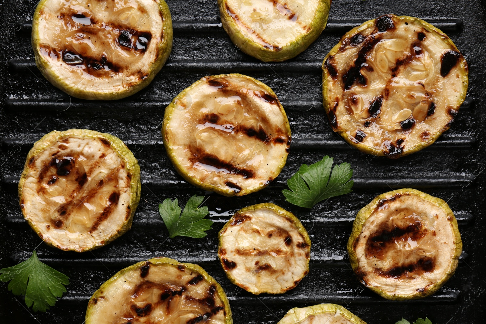 Photo of Tasty grilled zucchini slices with parsley on frying pan, flat lay