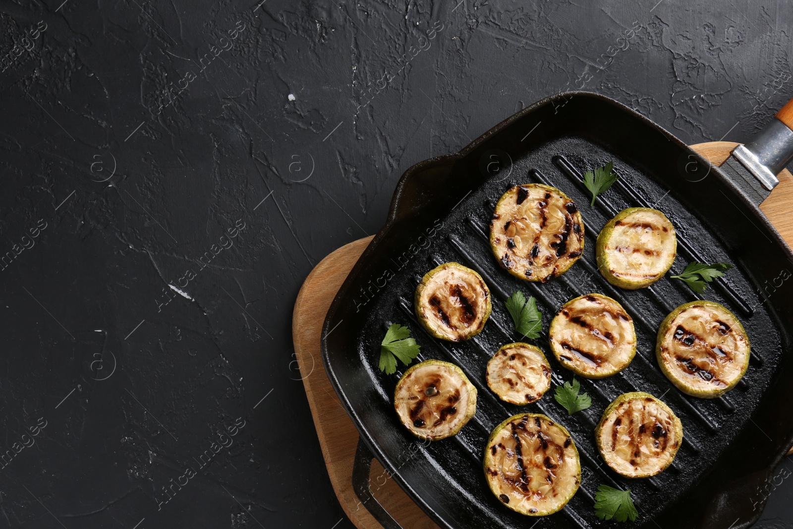 Photo of Tasty grilled zucchini slices with parsley in frying pan on grey textured table, top view. Space for text