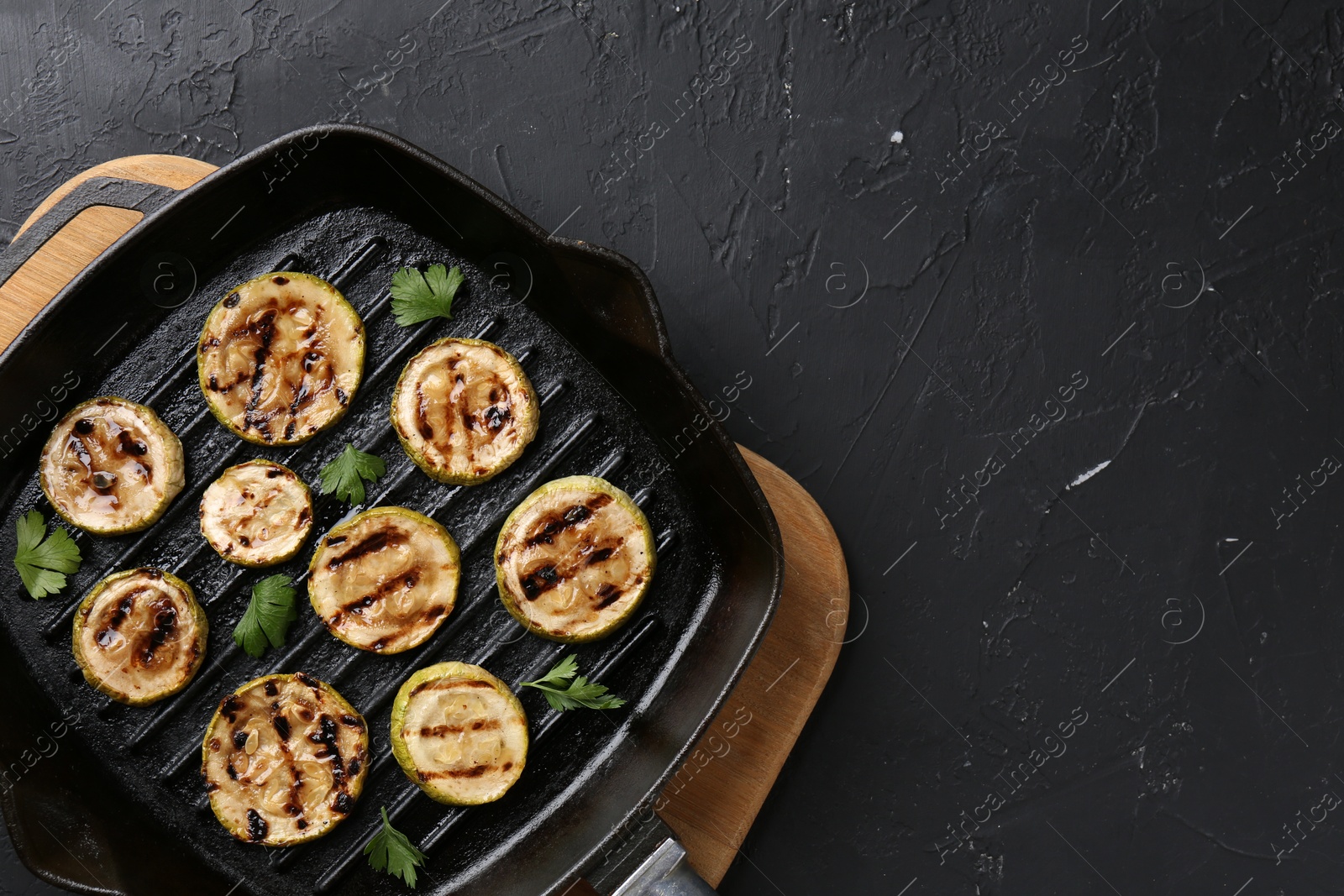 Photo of Tasty grilled zucchini slices with parsley in frying pan on grey textured table, top view. Space for text