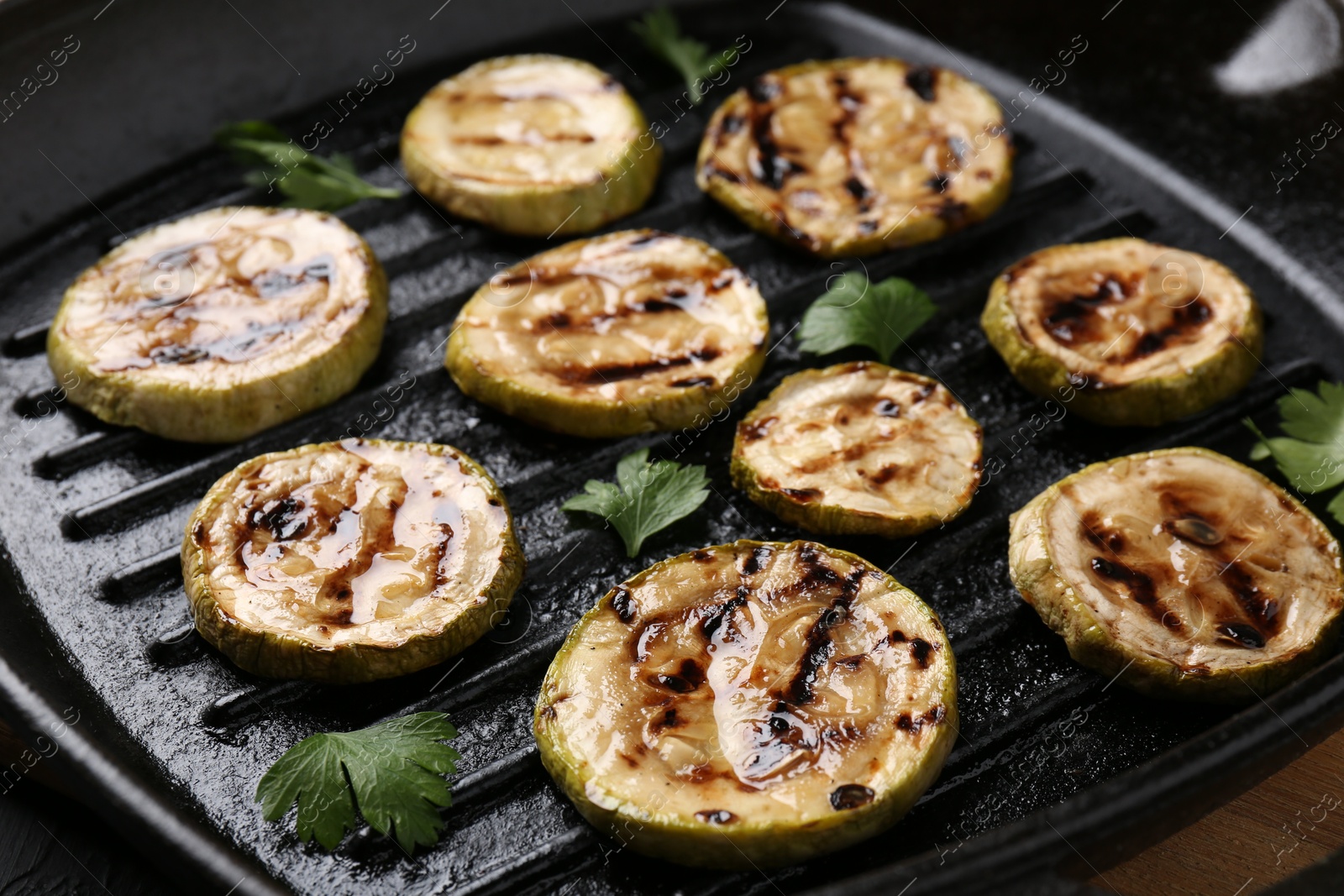 Photo of Tasty grilled zucchini slices with parsley in frying pan on grey table, closeup