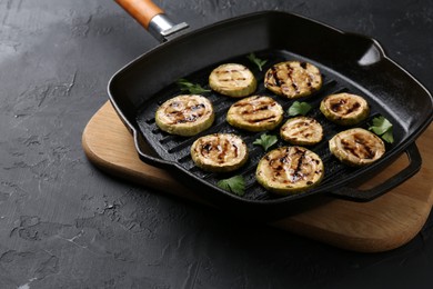 Photo of Tasty grilled zucchini slices with parsley in frying pan on grey textured table