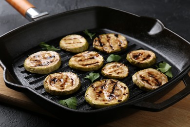 Photo of Tasty grilled zucchini slices with parsley in frying pan on grey table, closeup