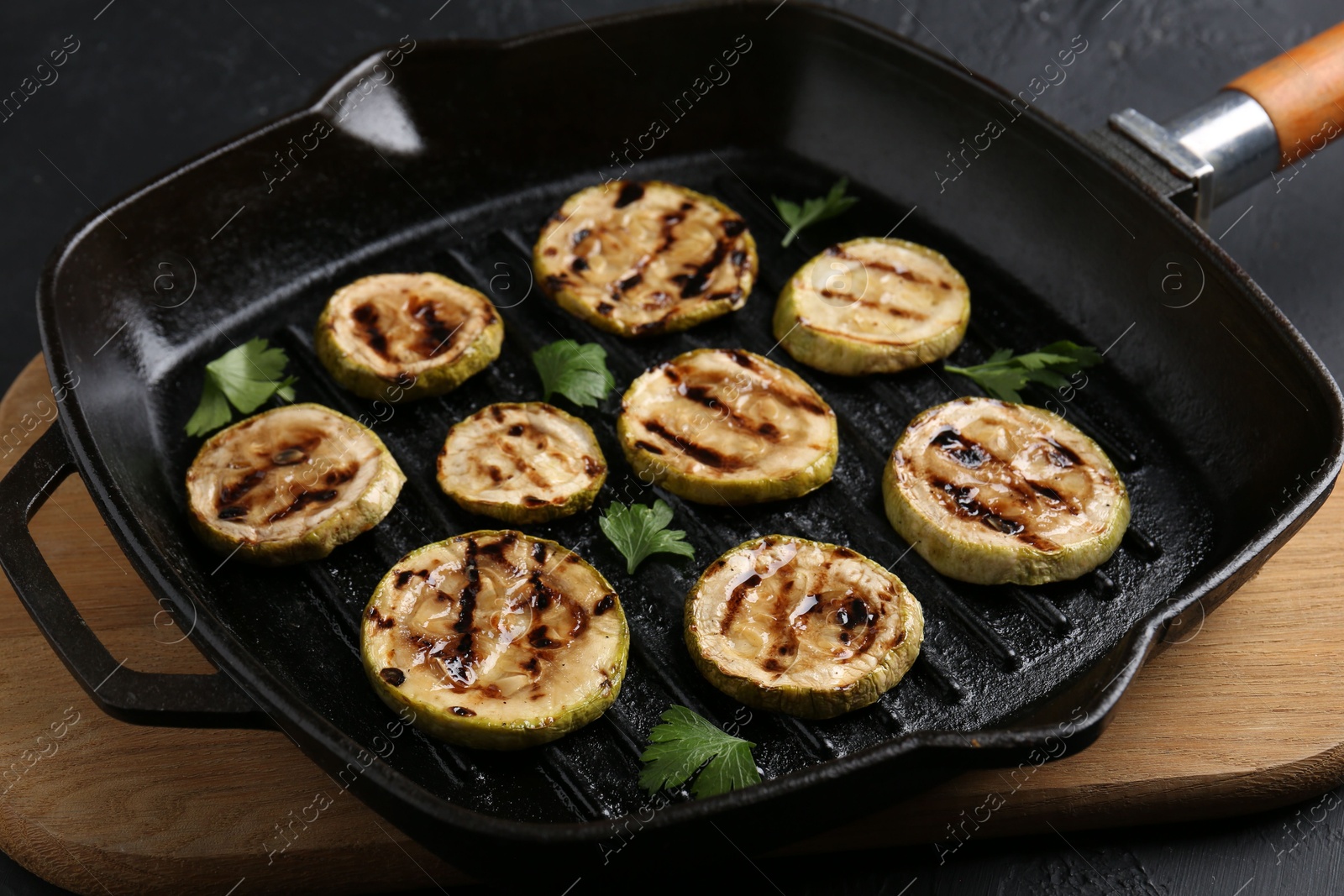 Photo of Tasty grilled zucchini slices with parsley in frying pan on grey table