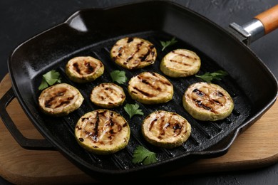 Photo of Tasty grilled zucchini slices with parsley in frying pan on grey table