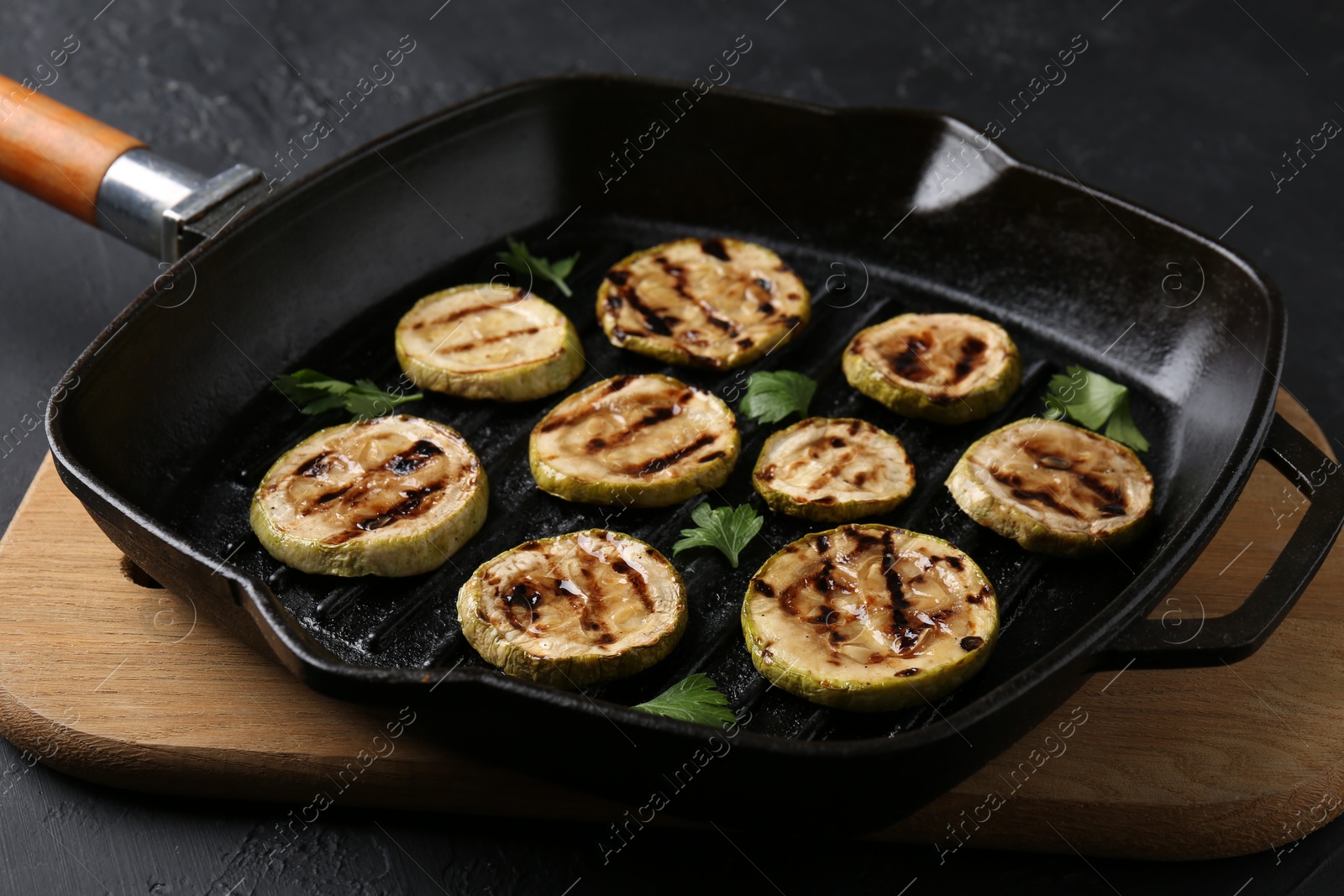 Photo of Tasty grilled zucchini slices with parsley in frying pan on grey table