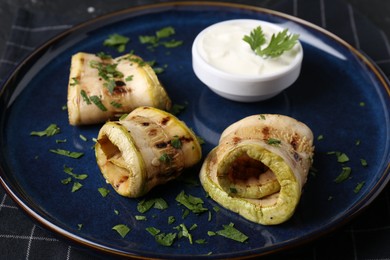 Photo of Tasty grilled zucchini slices served with sauce on table, closeup