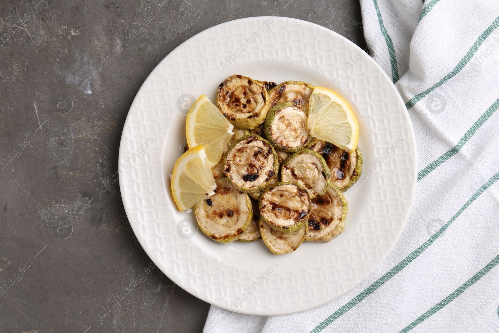 Photo of Tasty grilled courgette slices with lemon on grey textured table, top view