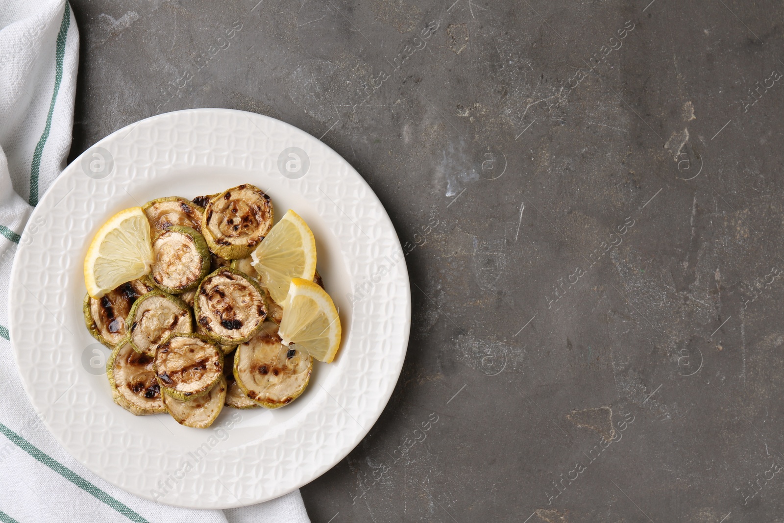 Photo of Tasty grilled courgette slices with lemon on grey textured table, top view. Space for text