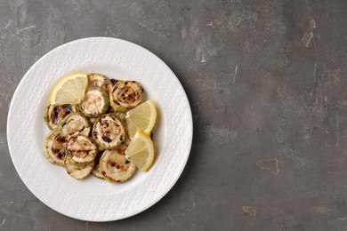 Tasty grilled courgette slices with lemon on grey textured table, top view. Space for text