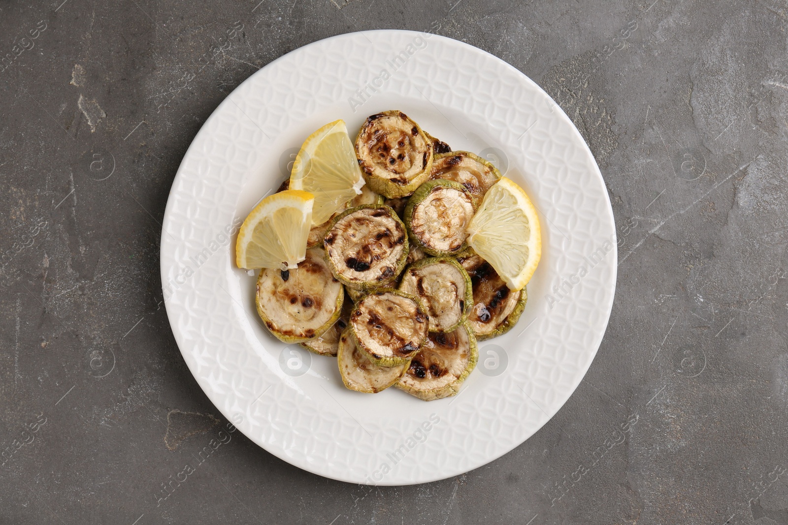 Photo of Tasty grilled courgette slices with lemon on grey textured table, top view