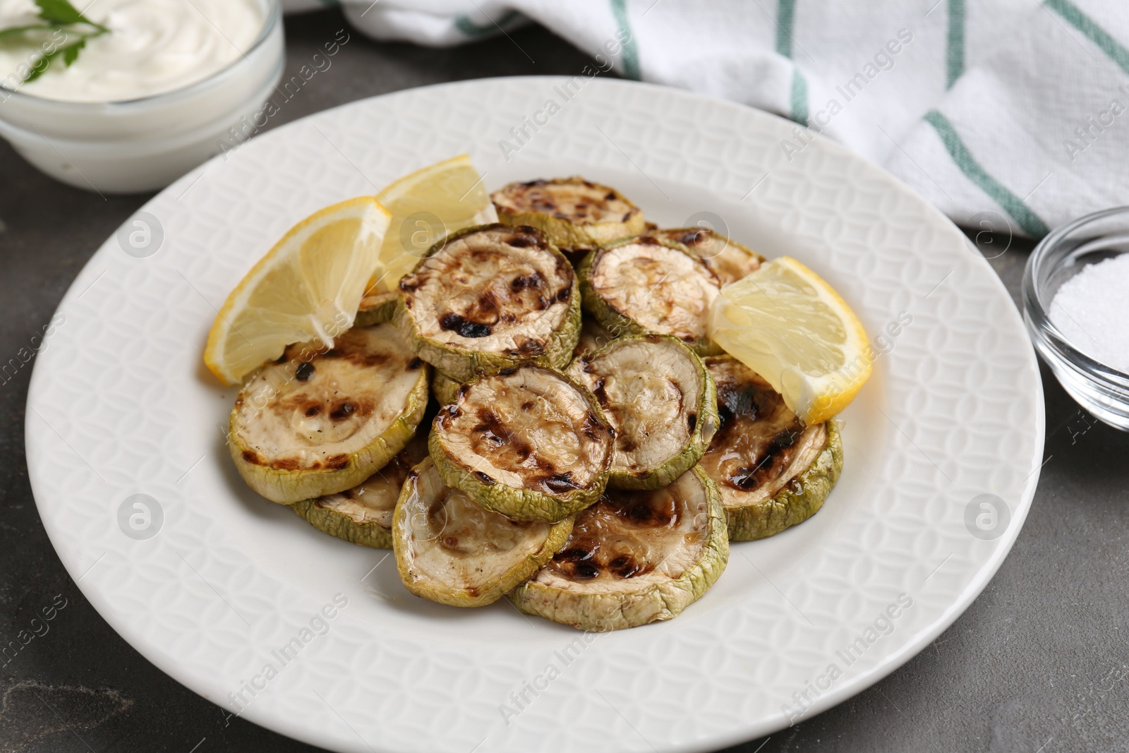 Photo of Tasty grilled courgette slices with lemon on grey table