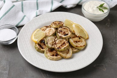 Photo of Tasty grilled courgette slices with lemon on grey textured table