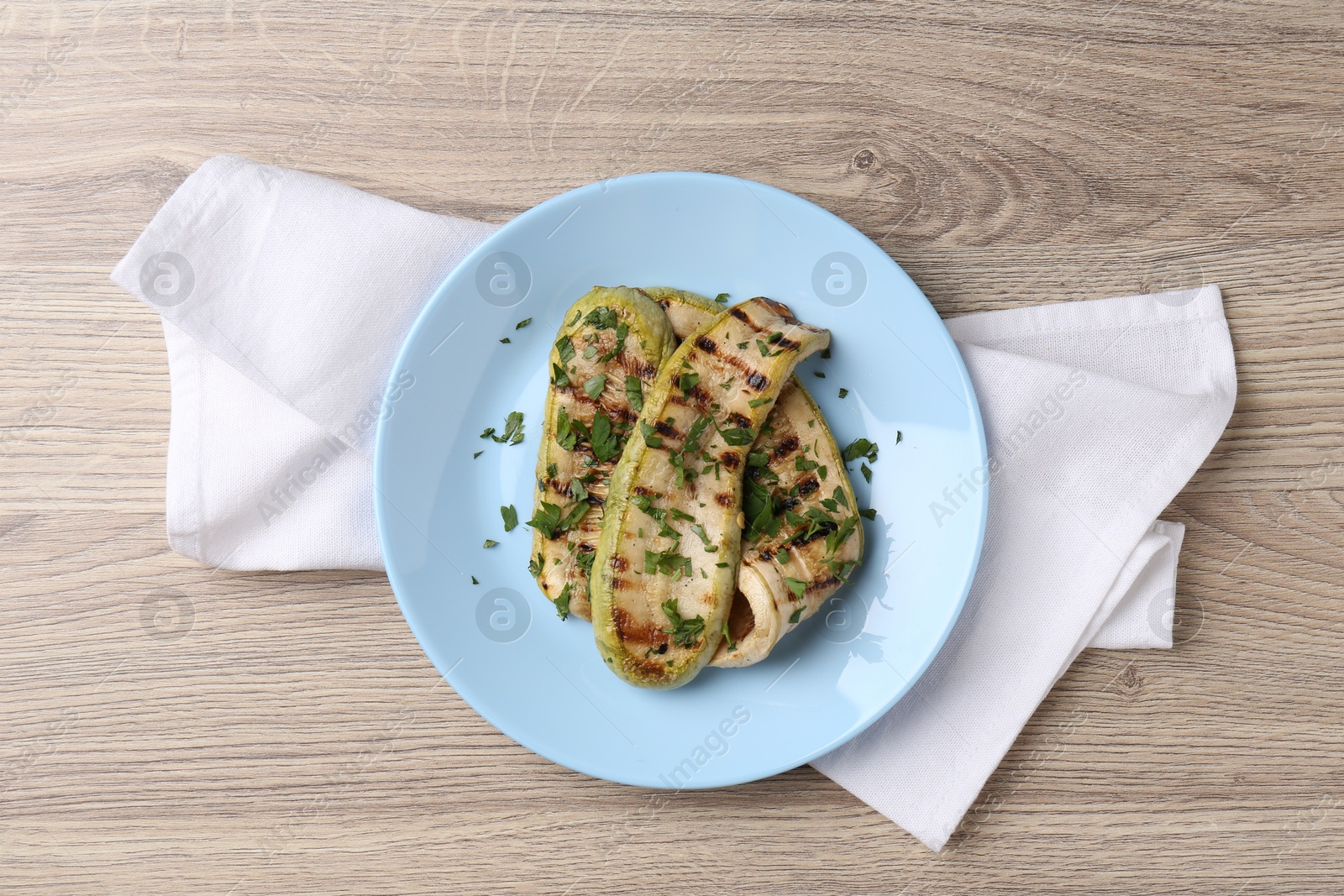 Photo of Tasty grilled courgette slices with parsley on wooden table, top view