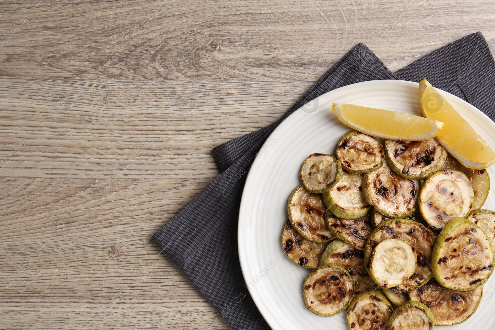 Photo of Tasty grilled courgette slices with lemon on wooden table, top view. Space for text