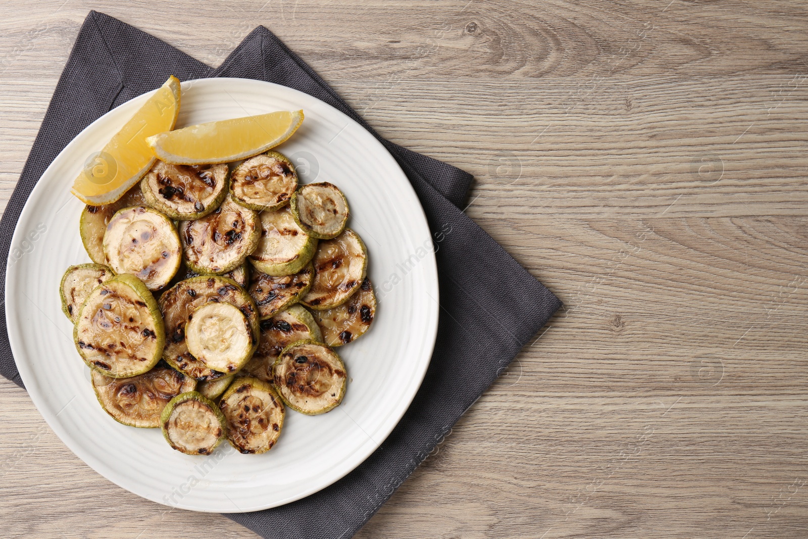 Photo of Tasty grilled courgette slices with lemon on wooden table, top view. Space for text