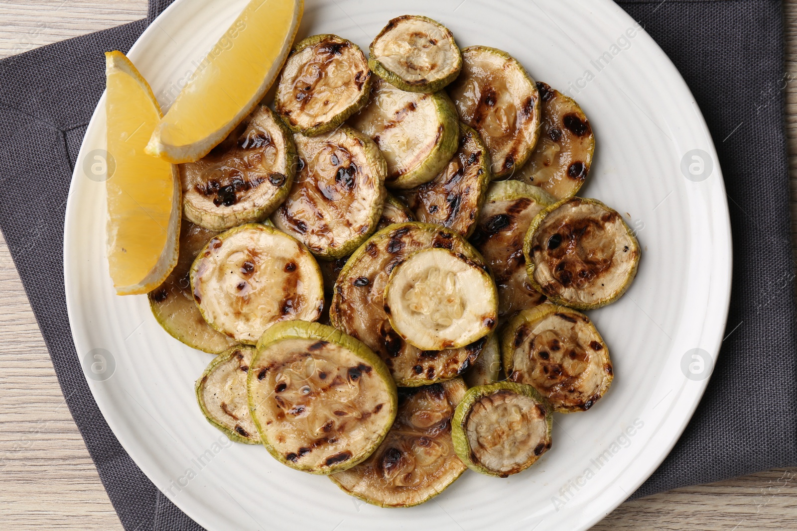 Photo of Tasty grilled courgette slices with lemon on wooden table, top view