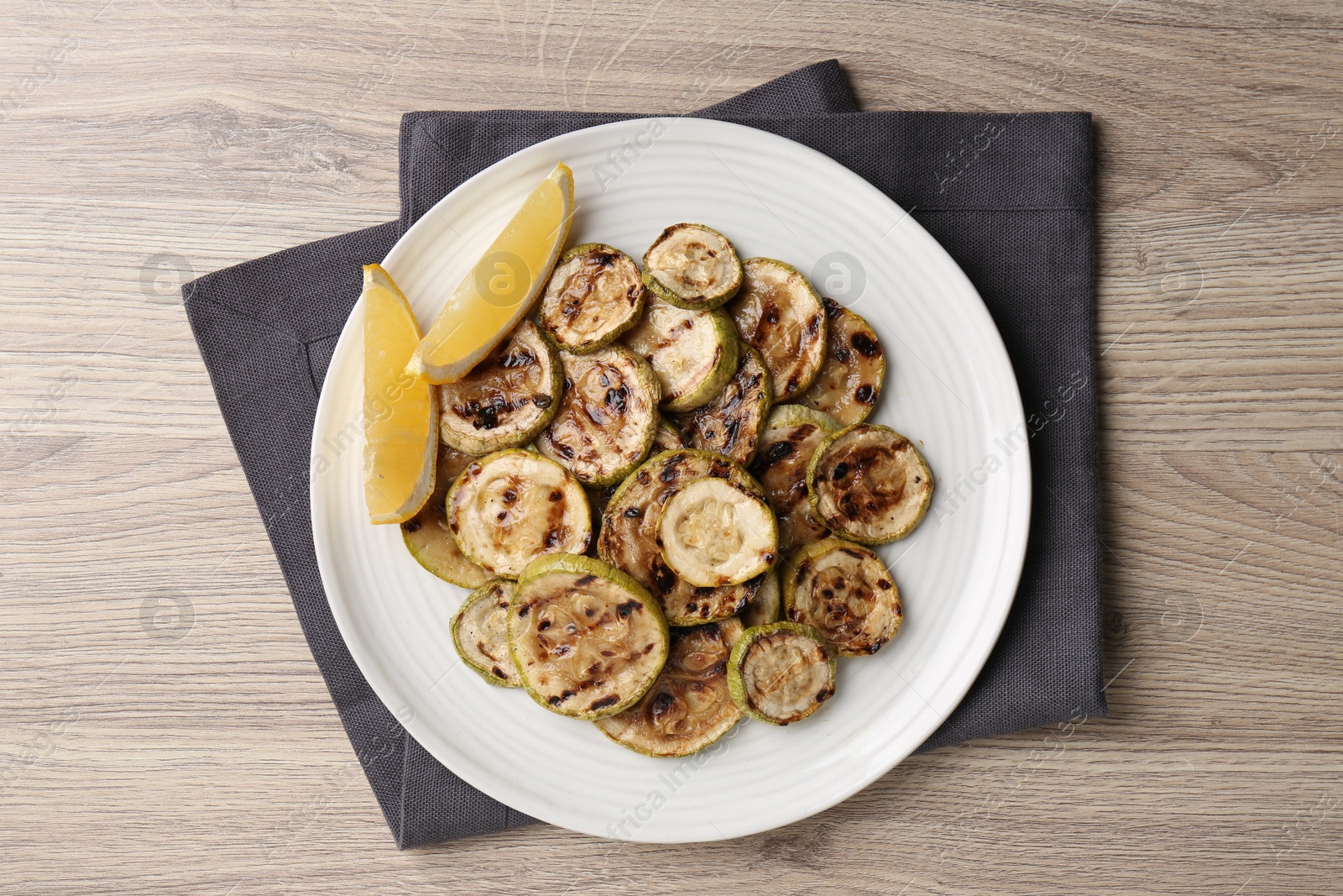 Photo of Tasty grilled courgette slices with lemon on wooden table, top view