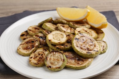 Photo of Tasty grilled courgette slices with lemon on wooden table, closeup