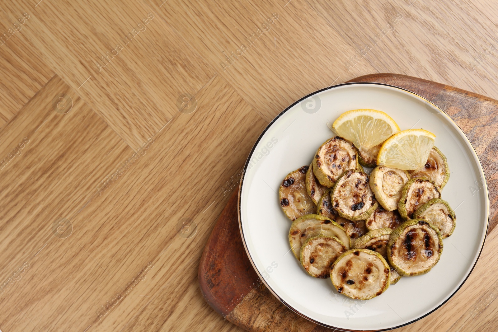 Photo of Tasty grilled courgette slices with lemon on wooden table, top view. Space for text