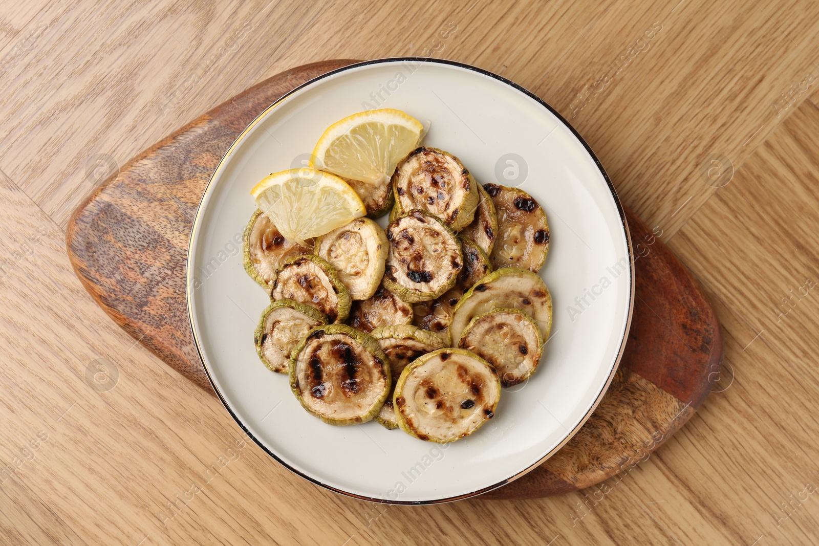 Photo of Tasty grilled courgette slices with lemon on wooden table, top view