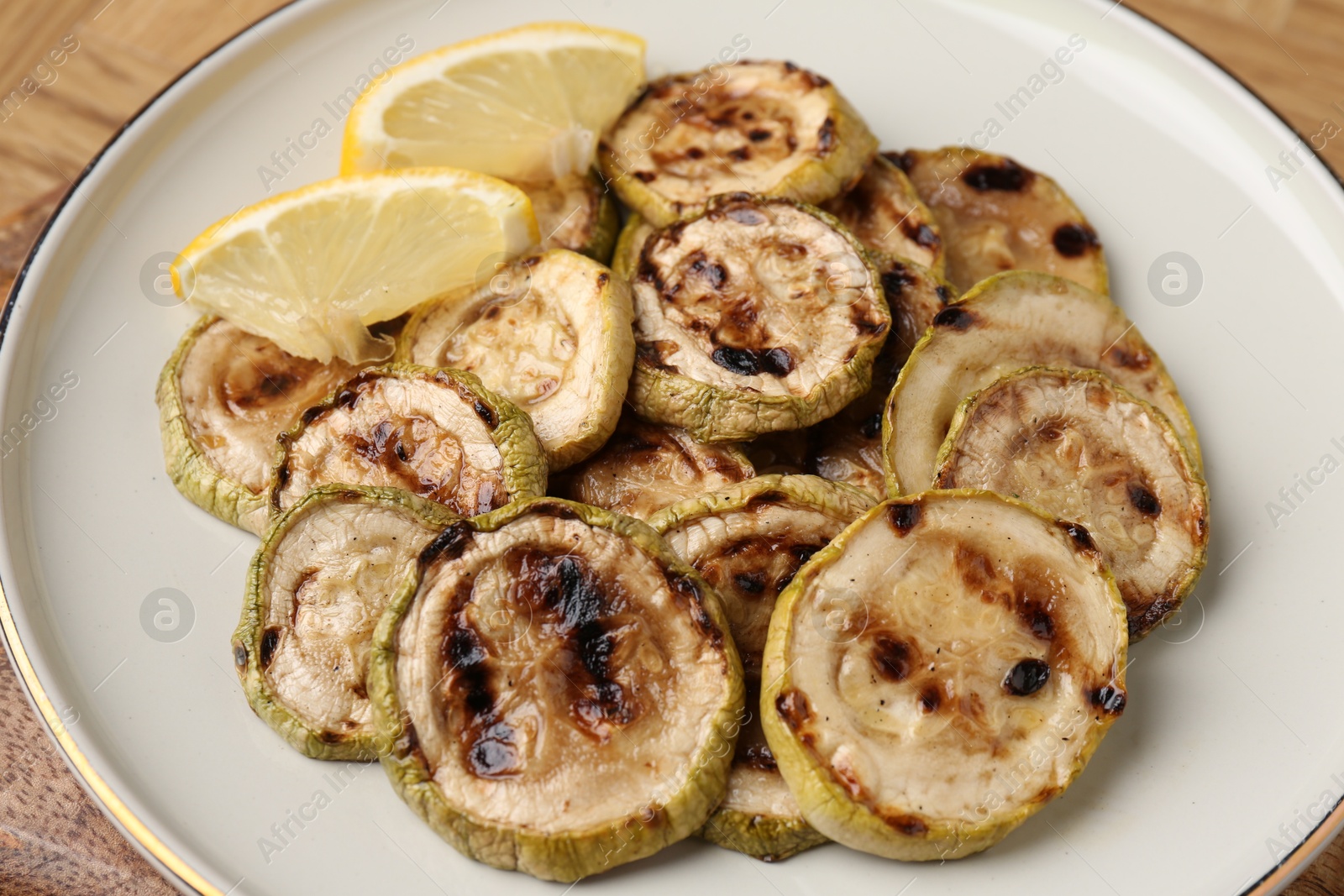 Photo of Tasty grilled courgette slices with lemon on table, closeup