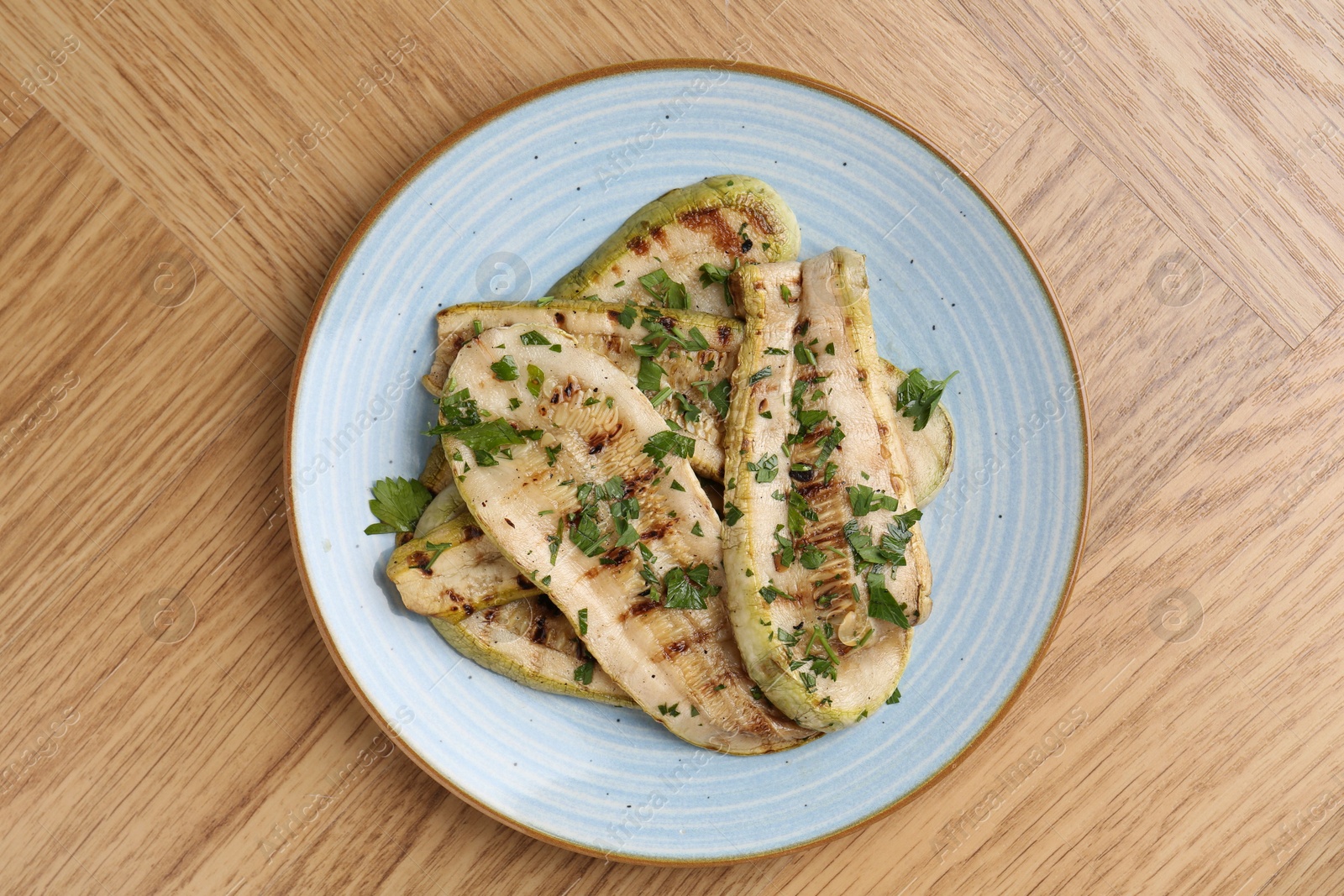 Photo of Tasty grilled courgette slices with parsley on wooden table, top view