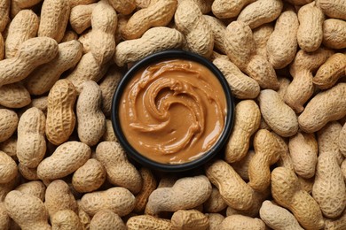 Photo of Tasty peanut butter in bowl among groundnuts, flat lay