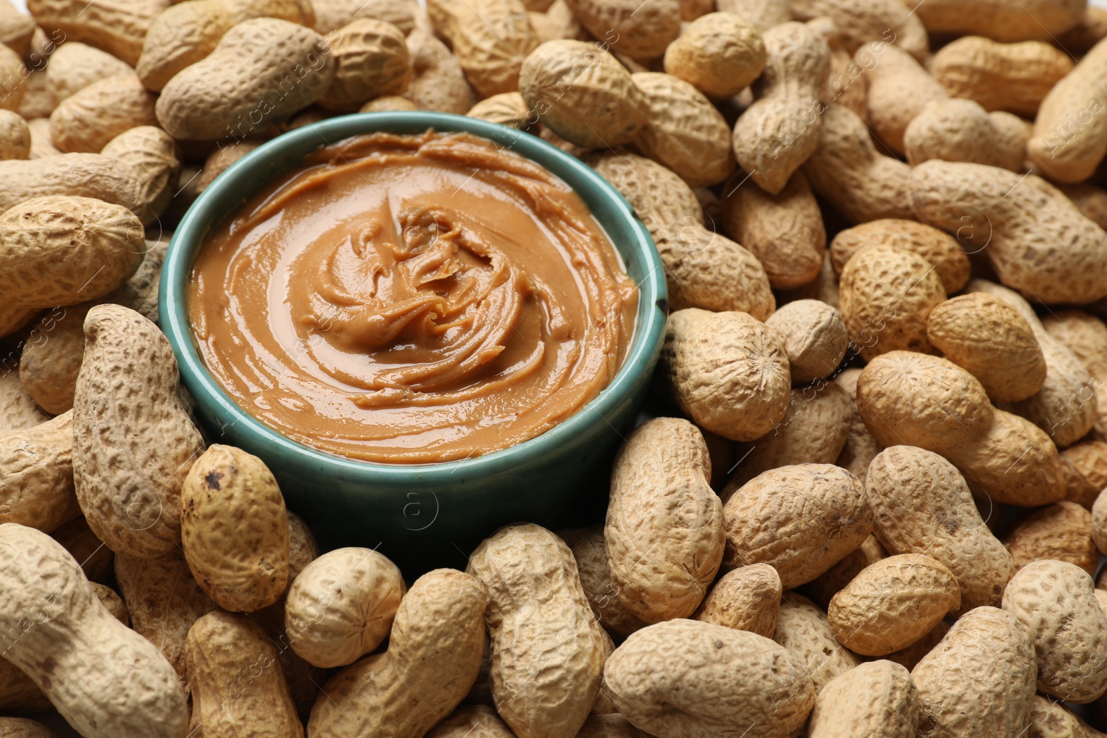 Photo of Tasty peanut butter in bowl among groundnuts