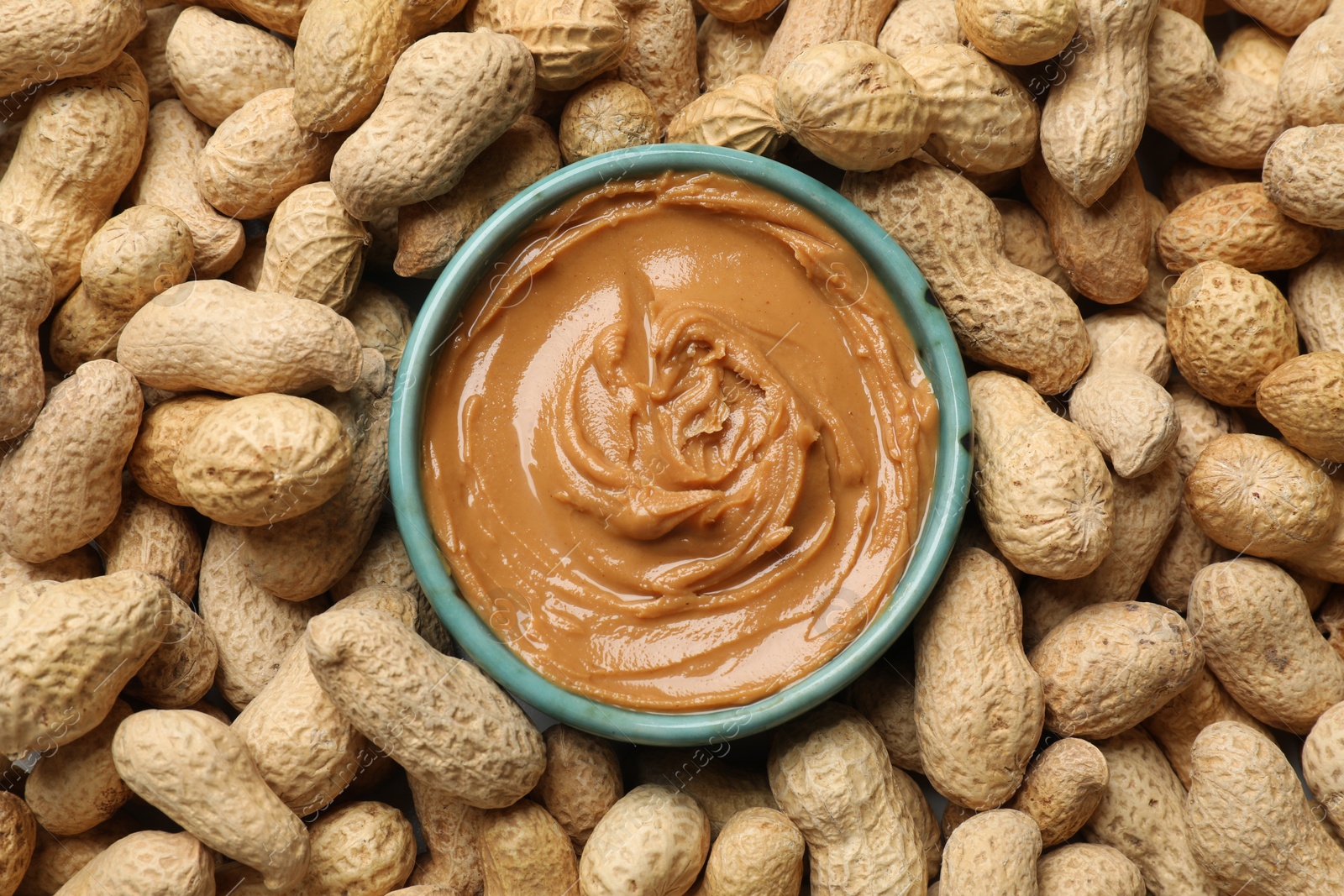 Photo of Tasty peanut butter in bowl among groundnuts, flat lay