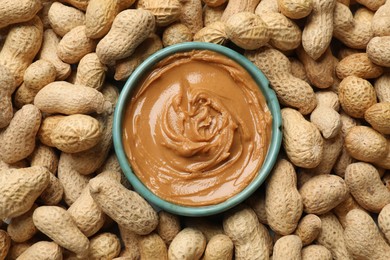 Photo of Tasty peanut butter in bowl among groundnuts, flat lay