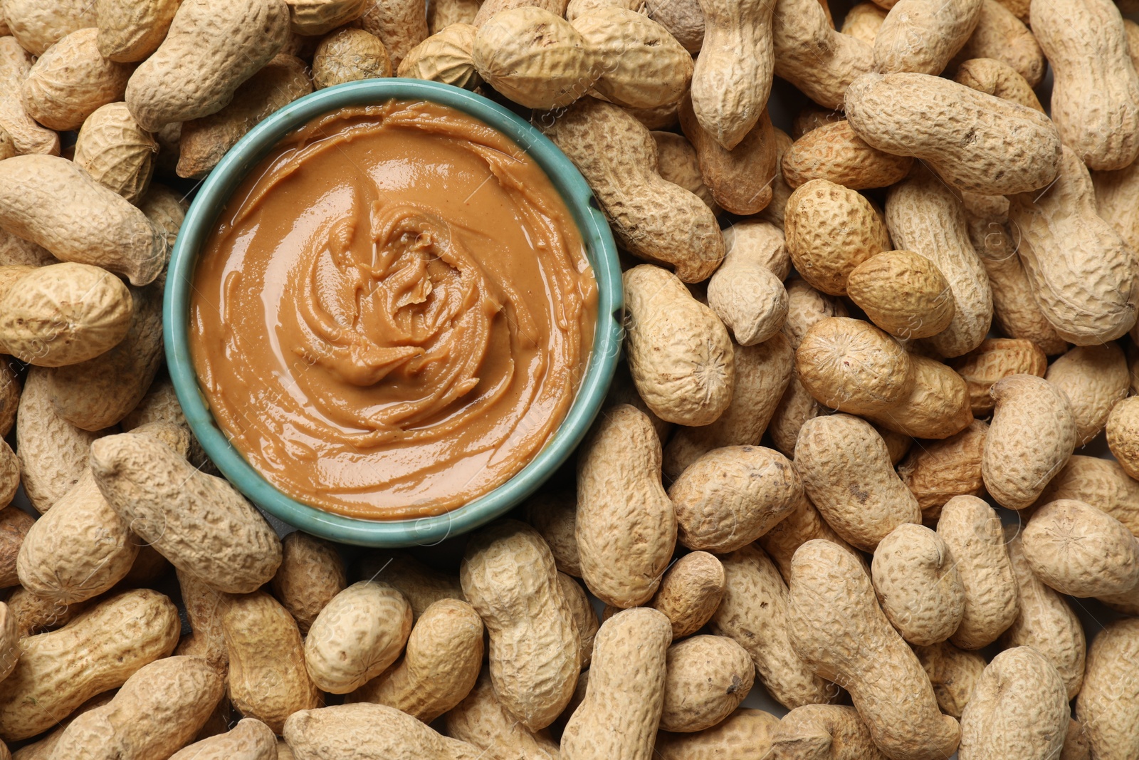 Photo of Tasty peanut butter in bowl among groundnuts, flat lay. Space for text