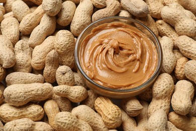 Photo of Tasty peanut butter in bowl among groundnuts