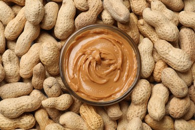 Photo of Tasty peanut butter in bowl among groundnuts, flat lay