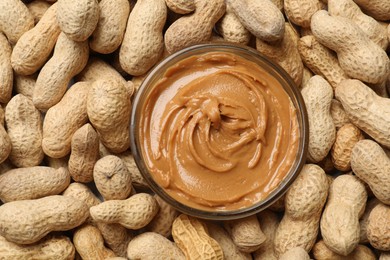 Photo of Tasty peanut butter in bowl among groundnuts, flat lay