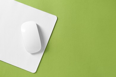 Wireless mouse and mousepad on green background, top view. Space for text