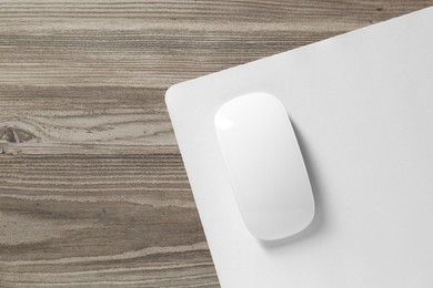 Wireless mouse and mousepad on wooden table, top view. Space for text