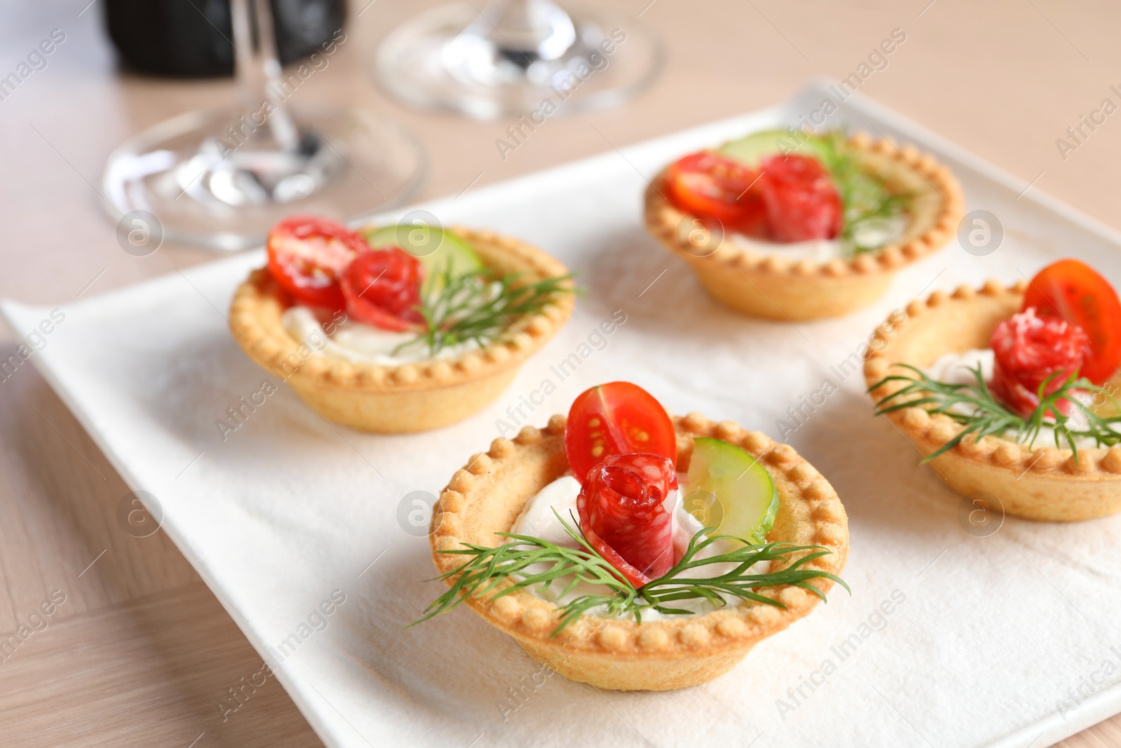 Photo of Delicious canapes with dry smoked sausages, cream cheese and vegetables on wooden table, closeup