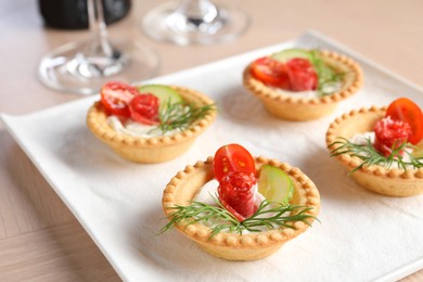 Photo of Delicious canapes with dry smoked sausages, cream cheese and vegetables on wooden table, closeup