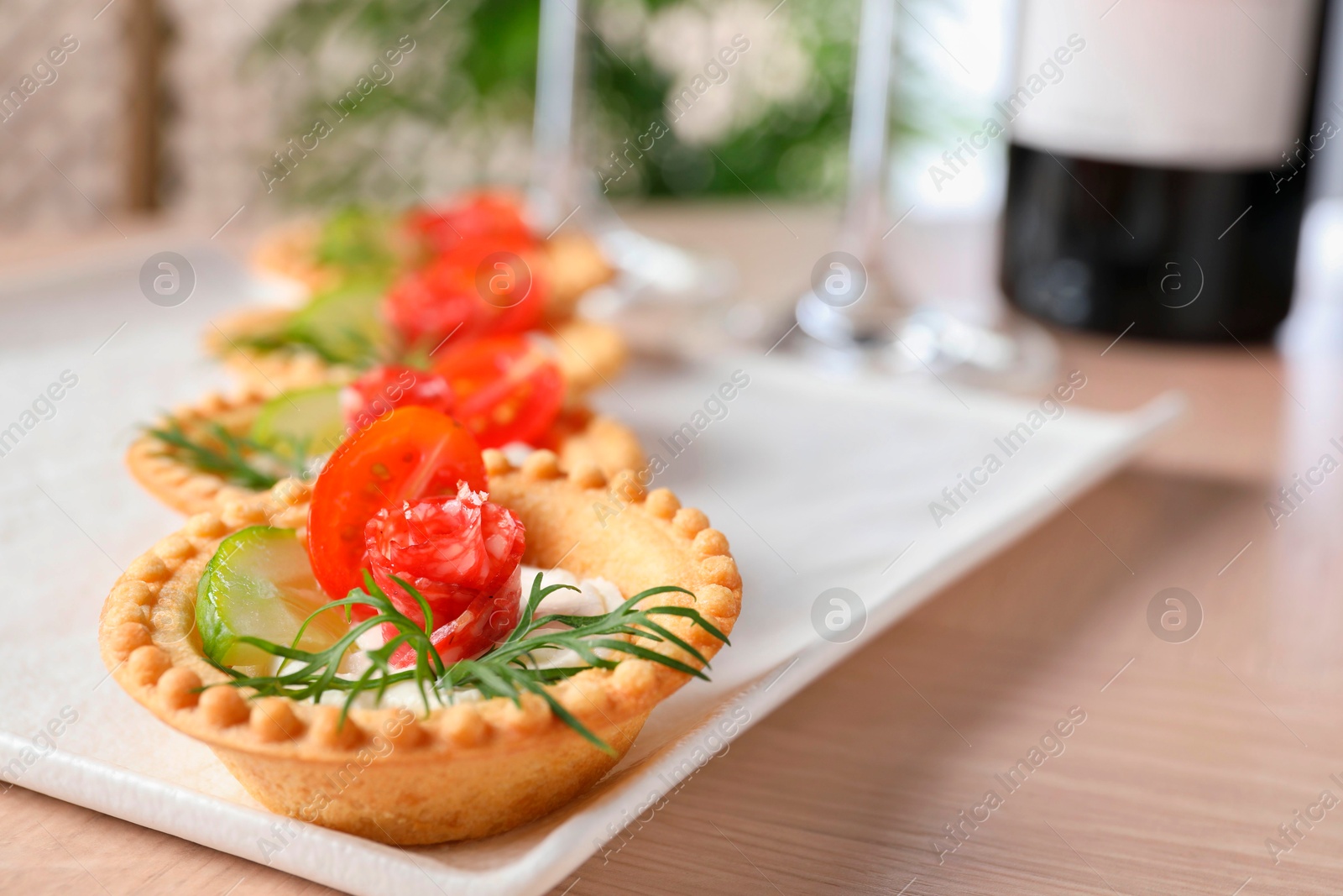 Photo of Delicious canapes with dry smoked sausages, cream cheese and vegetables on wooden table, closeup