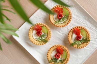 Delicious canapes with dry smoked sausages, cream cheese and vegetables on wooden table, top view