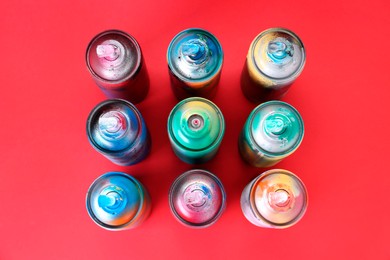 Many spray paint cans on red background, flat lay