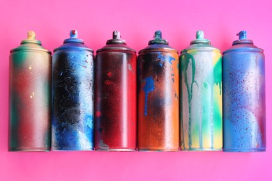 Photo of Many spray paint cans on pink background, flat lay