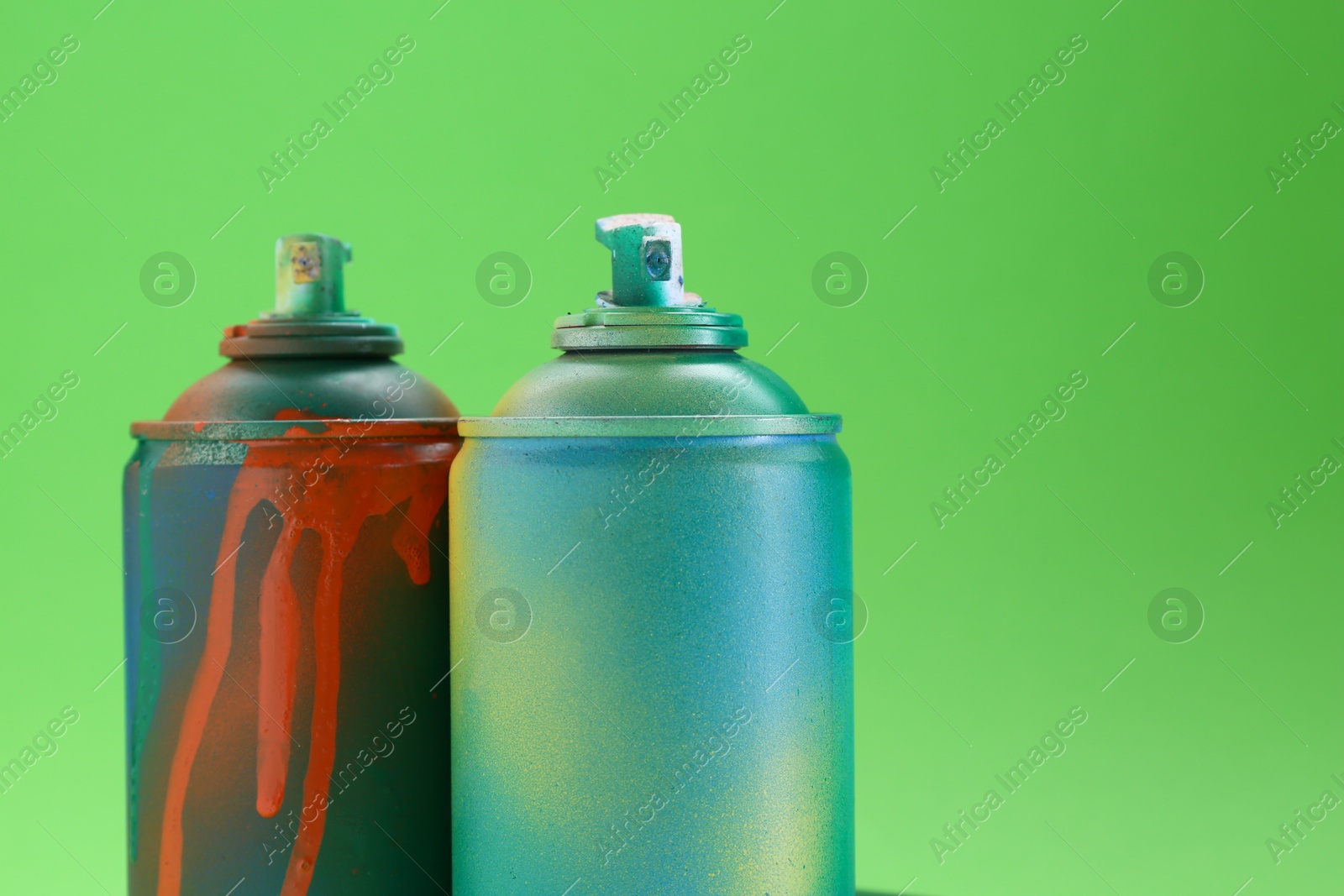 Photo of Bright spray paint cans on green background, closeup