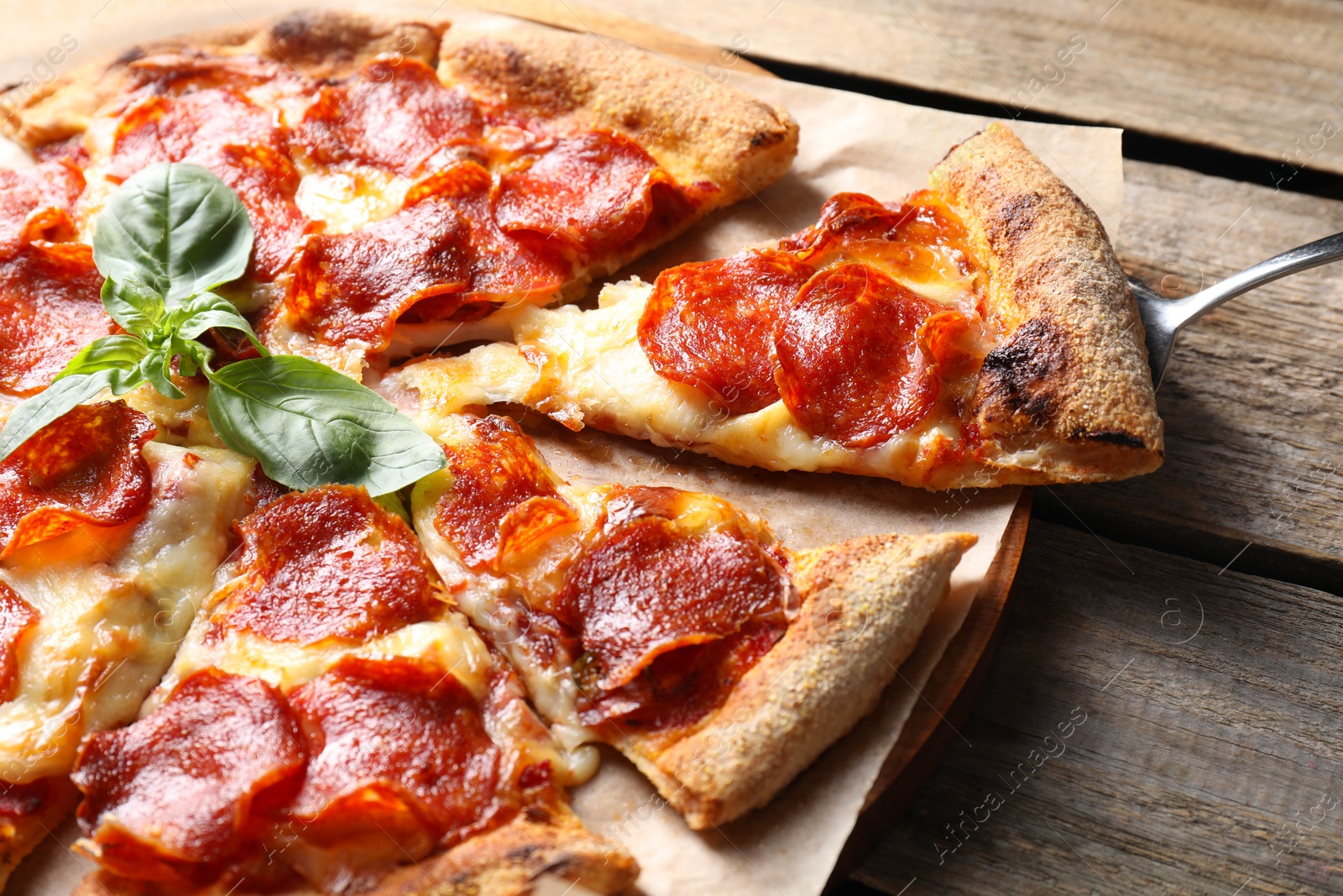 Photo of Tasty pepperoni pizza with basil on wooden table, closeup