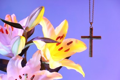 Photo of One cross with chain and beautiful lily flowers on purple background, closeup. Religion of Christianity