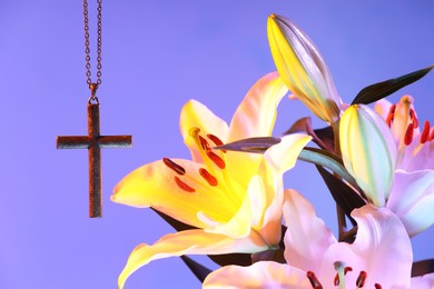 Photo of One cross with chain and beautiful lily flowers on purple background, closeup. Religion of Christianity